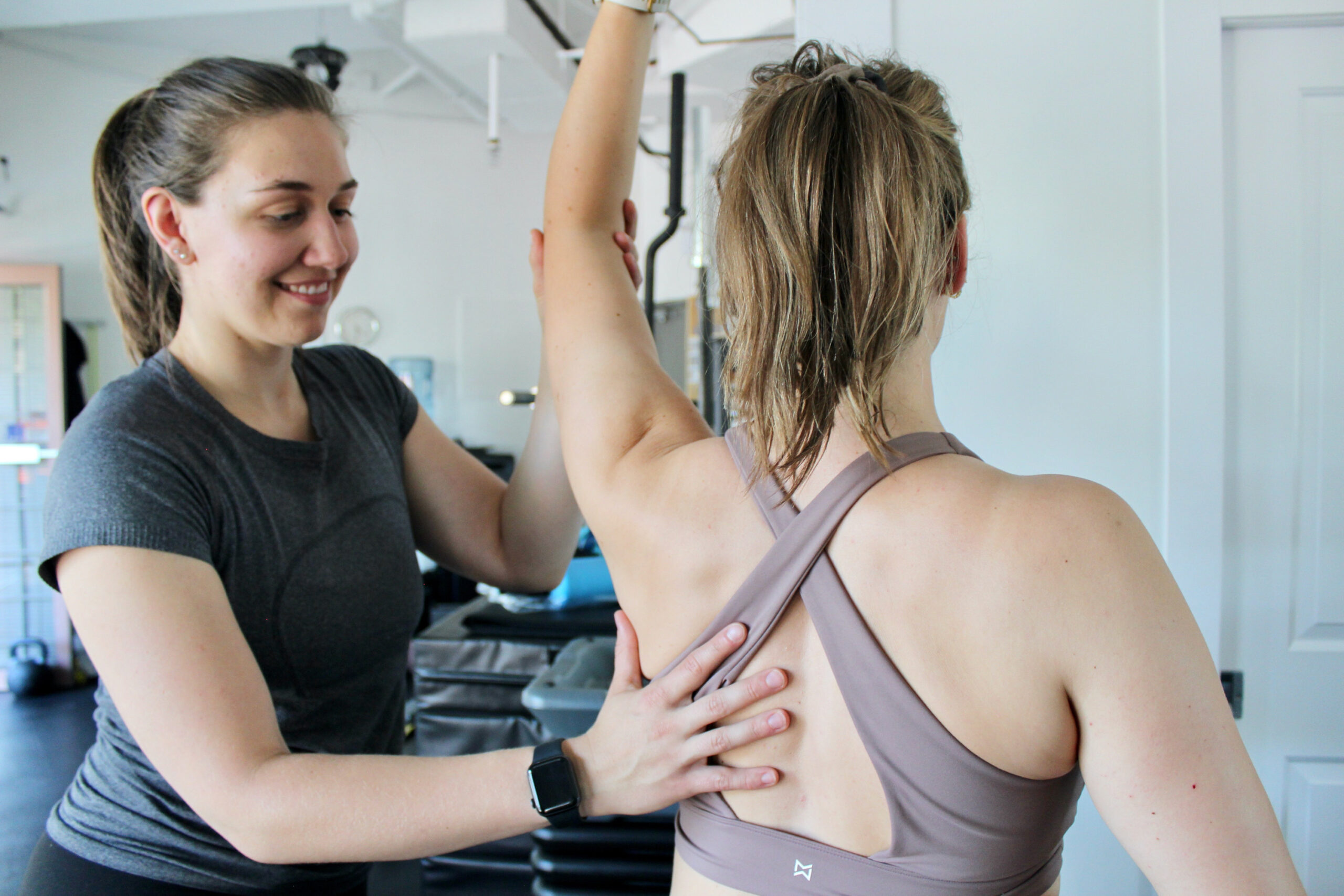 A fitness instructor assists a woman in a sports bra during a physical therapy session focused on mobility and strength training, emphasizing Friday Health principles.