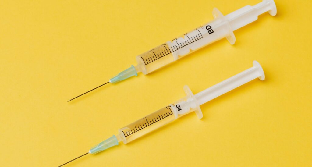 Two syringes on a yellow background, emphasizing medical and healthcare themes.