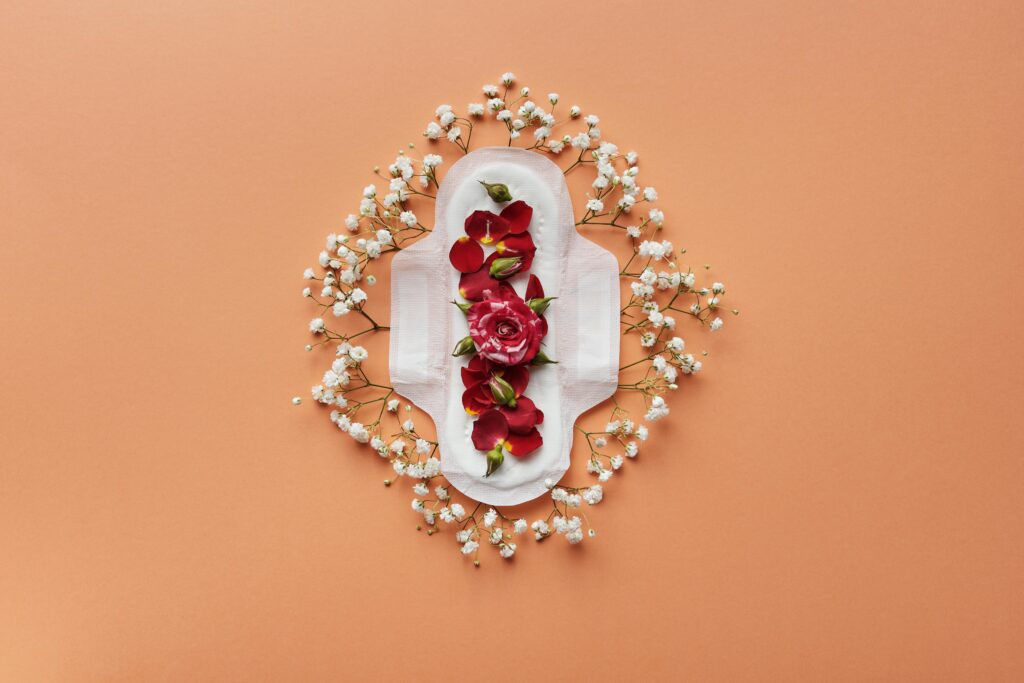 Artistic flatlay of a sanitary pad adorned with flowers on a peach background, symbolizing menstruation.