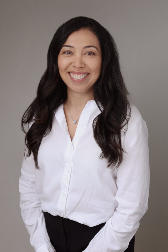 A smiling woman with long dark hair, wearing a white button-up shirt, stands against a neutral background. The image represents the concept of Friday Health, promoting wellness and positivity.