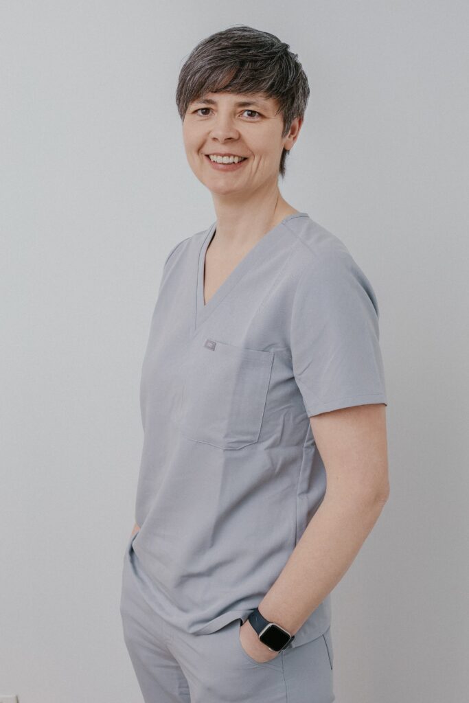 Alt text: A smiling healthcare professional wearing light gray scrubs and a smartwatch, promoting a friendly atmosphere at Friday Health.