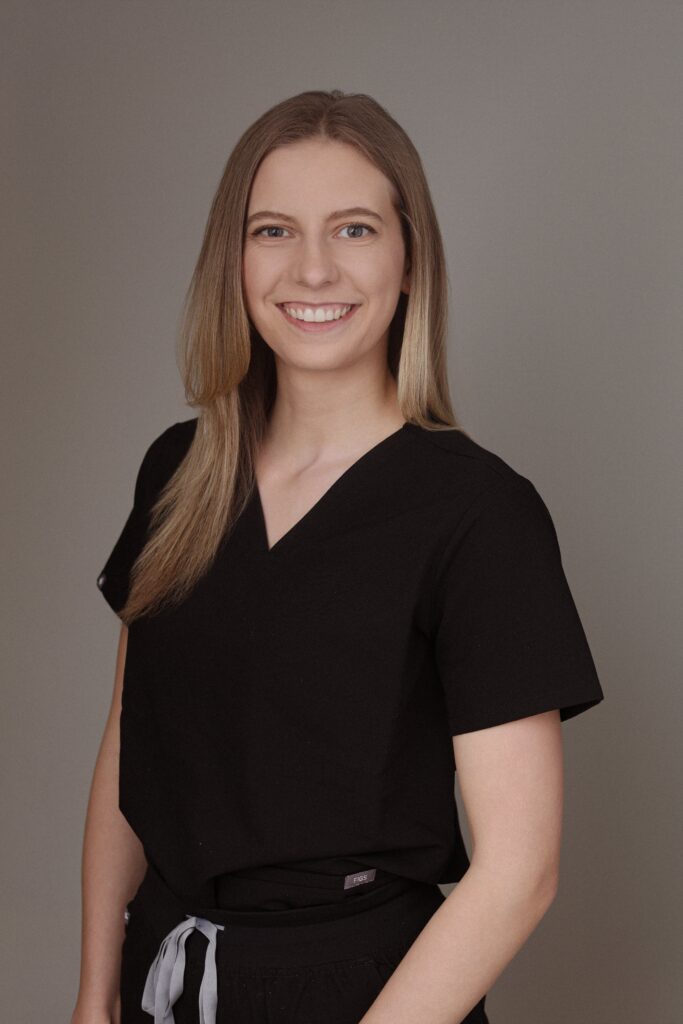 Alt text: A smiling woman wearing a black medical scrub top stands against a neutral background, representing Friday Health.
