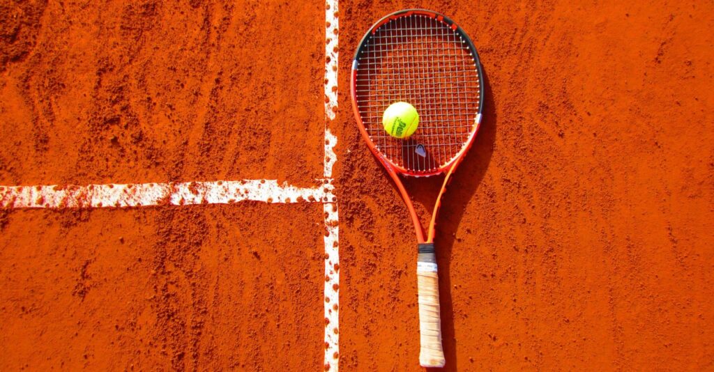 Tennis racket and ball on red clay court, ideal for sports-themed content.
