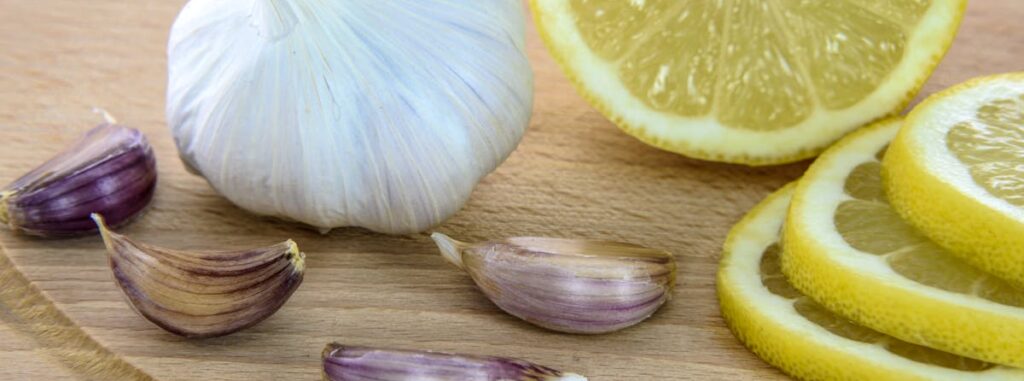 Close-up of fresh garlic and lemon slices on a wooden board, ideal for healthy cooking.