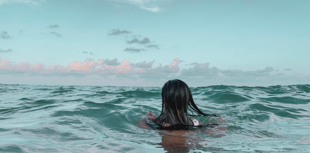 A woman swimming in the ocean, enjoying a sunny day with a beautiful sky.