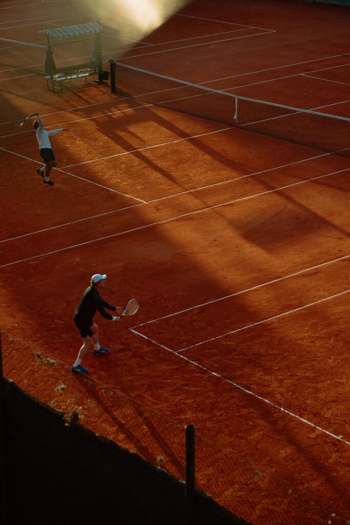 High-angle view of an active tennis game on a clay court during sunset, capturing dynamic play.