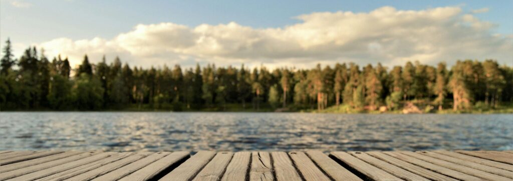 Serene wooden dock with a forested lake view under a bright summer sky in Sweden.