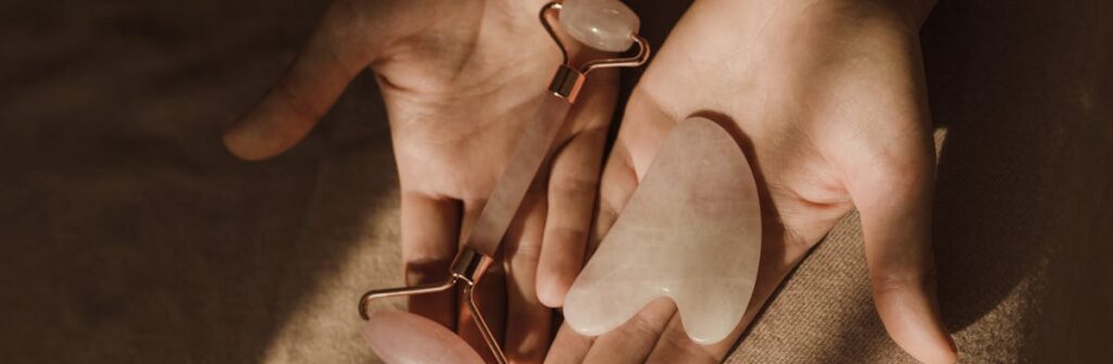 Close-up of hands holding a face roller and gua sha tool for skincare routine.