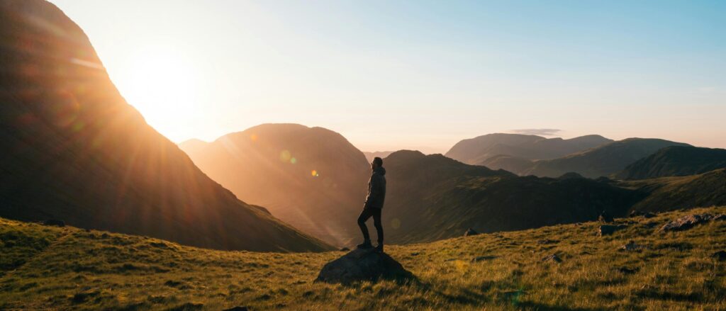 Silhouette of a person standing on a hill during sunrise in Cumbria, England with scenic mountain views.