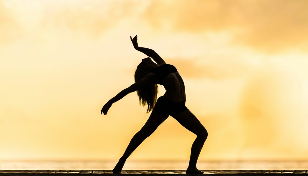 A dancer in a silhouetted pose stretches gracefully against a golden sunset, symbolizing vitality and movement, embodying the essence of Friday Health.