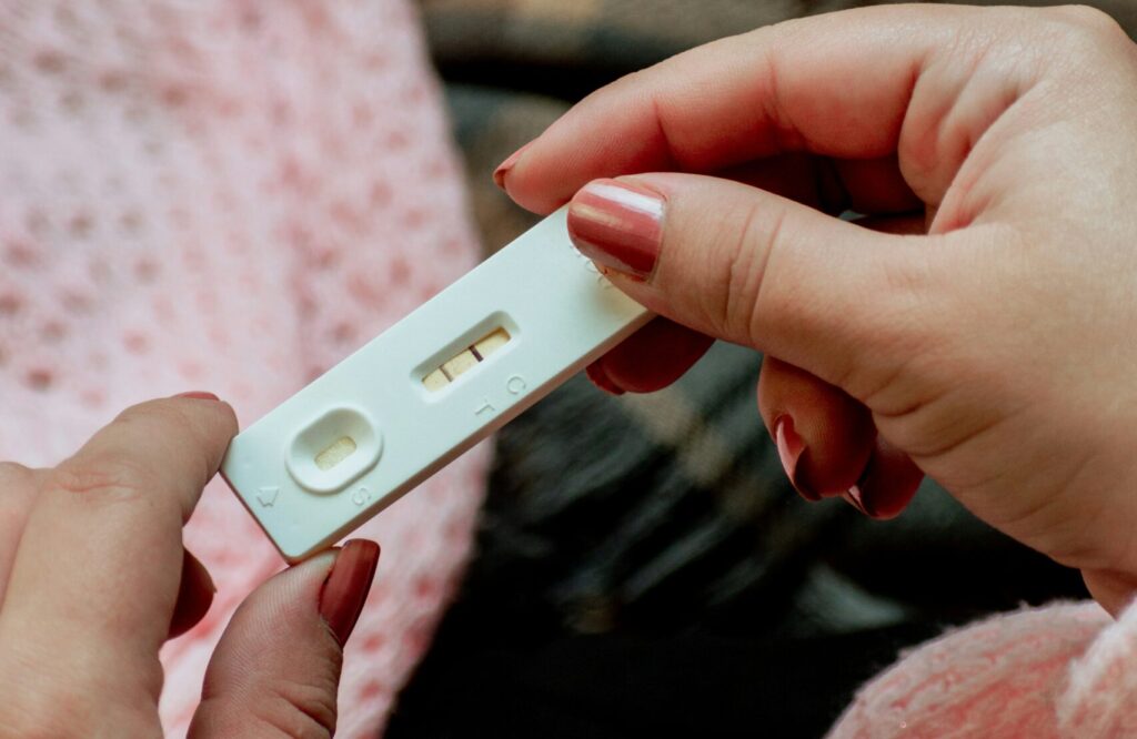 A close-up image of hands holding a pregnancy test, with the focus on the test results, set against a cozy background. The environment suggests a moment of contemplation regarding Friday Health.