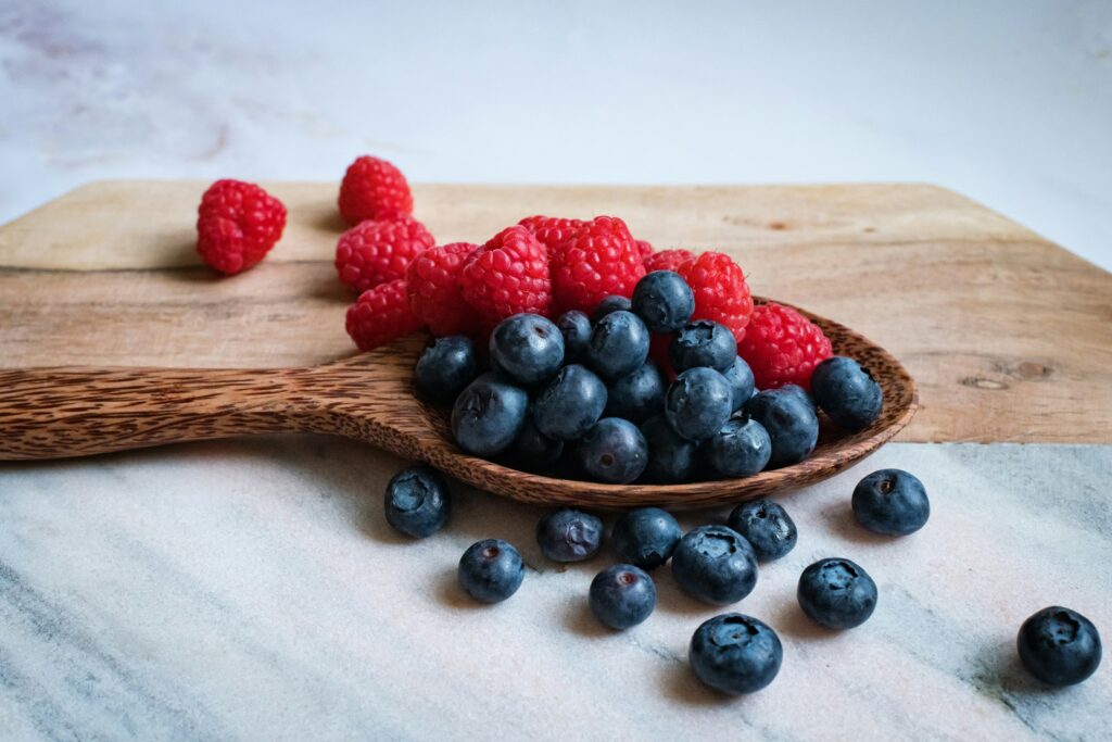 A wooden spoon holds an assortment of fresh blueberries and raspberries, placed on a light-colored marble surface, reflecting the vibrant colors of Friday Health by promoting healthy eating.