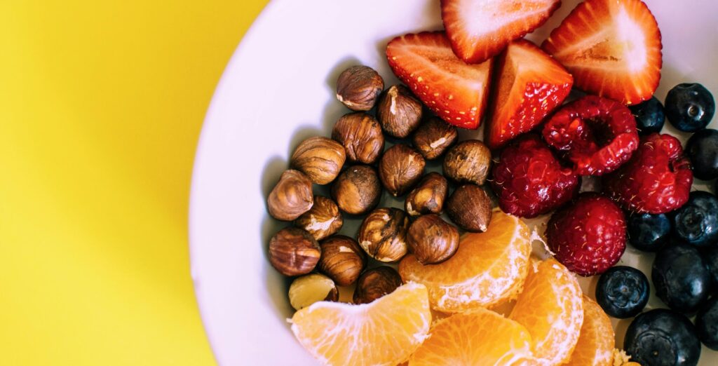 Close-up of a bowl with fresh fruits and nuts against a vibrant yellow backdrop.