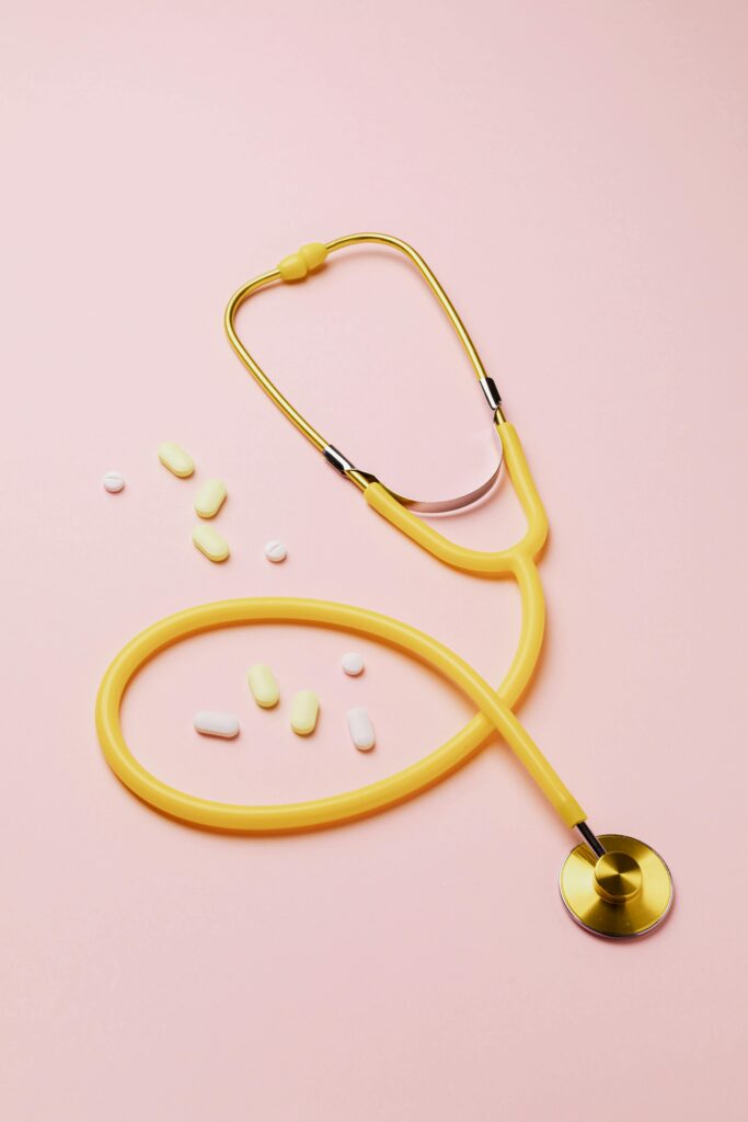 A yellow stethoscope and assorted pills on a pink background symbolize healthcare and treatment.