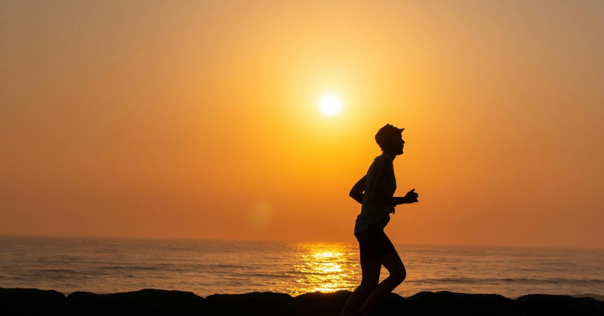 A silhouette of a person running along the ocean shore during a picturesque sunset.