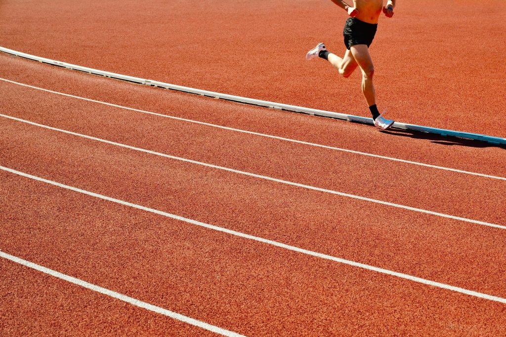 Athlete running on a red track in an outdoor stadium on a sunny day.