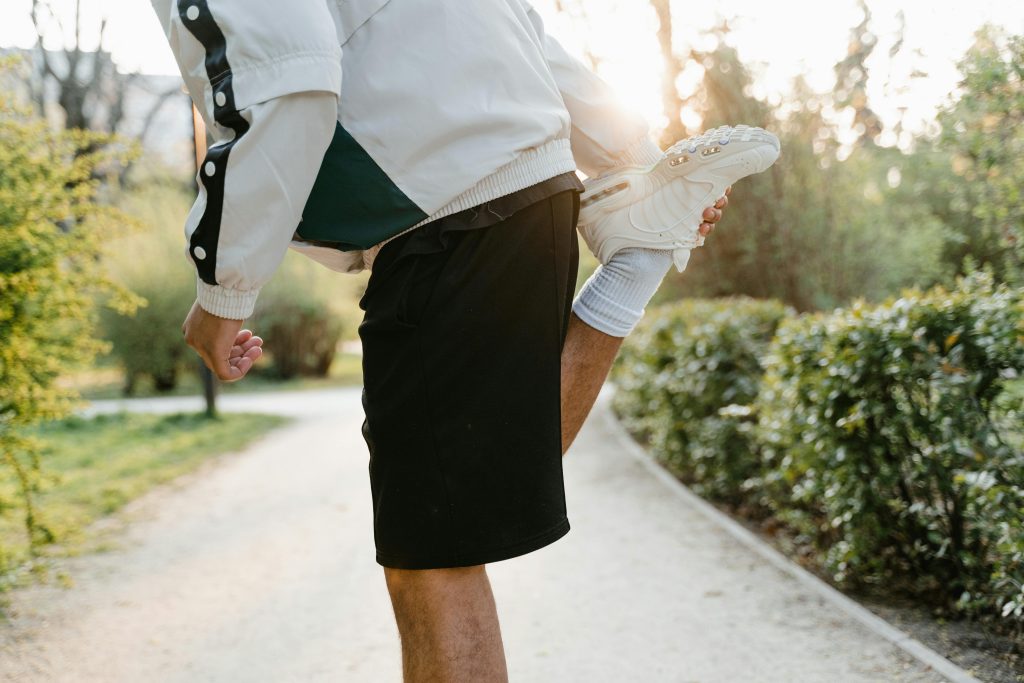 Close-up of a person stretching leg in a sunny outdoor park, ideal for fitness themes.