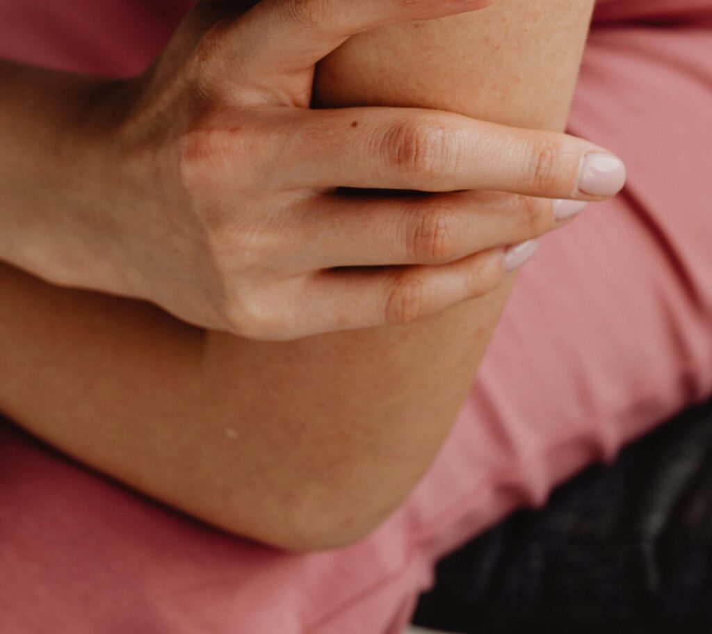 Close-up image of a female hand gently holding an elbow, showcasing skin texture and a minimalist manicure.