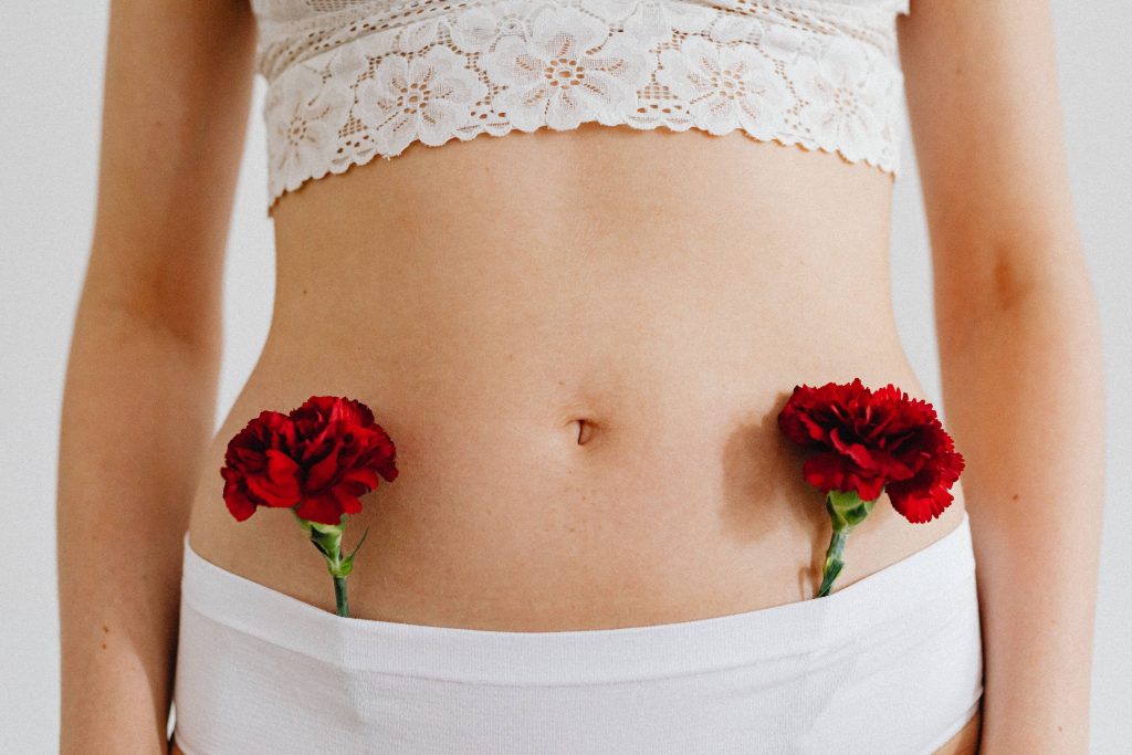 Conceptual close-up of red carnations placed on a human body in lace and underwear.