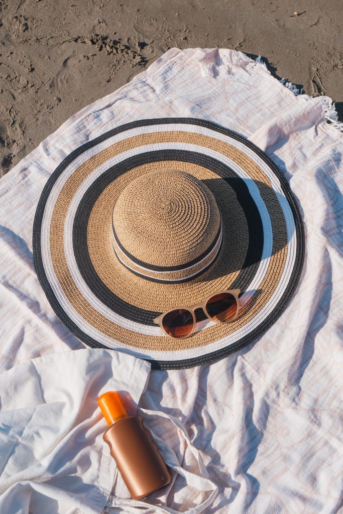 Close-up of beach essentials including sun hat, sunglasses, and sunscreen on blanket.