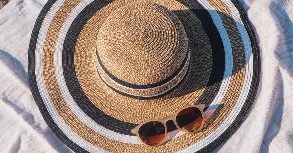 Close-up of beach essentials including sun hat, sunglasses, and sunscreen on blanket.
