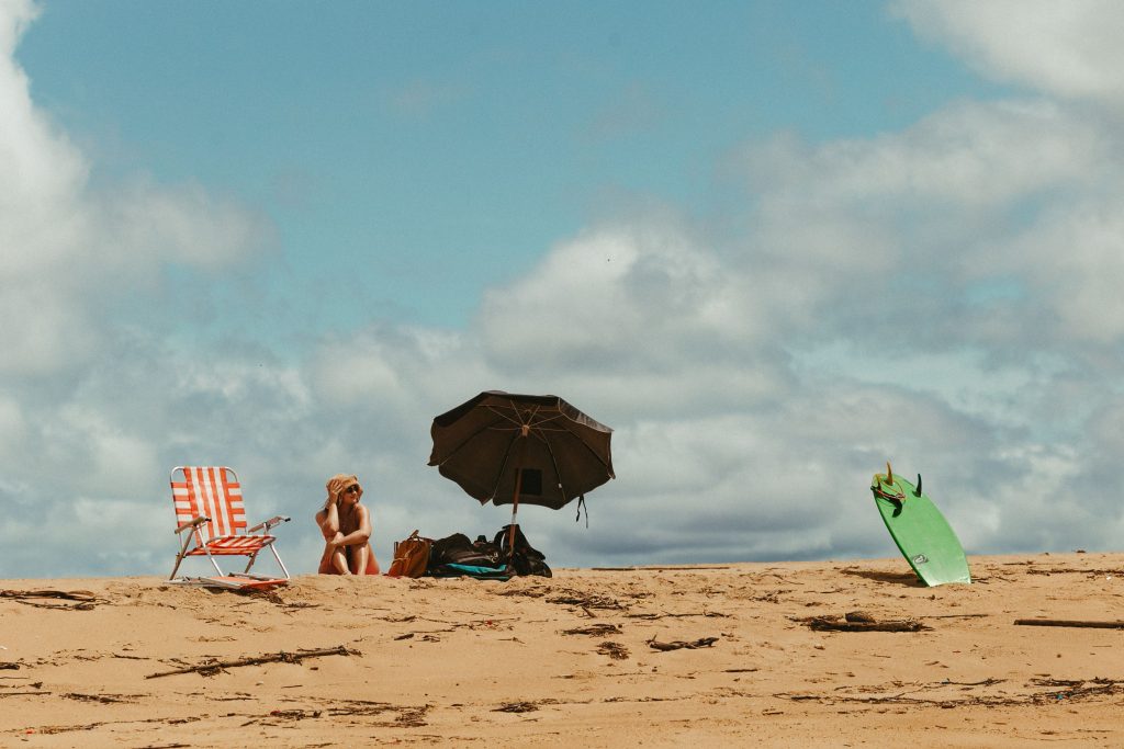 Person enjoying a sunny beach day with a chair, umbrella, and surfboard. Perfect summer vibe.